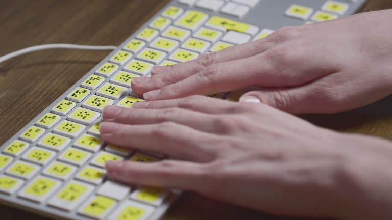 Close-up of a computer keyboard with braille. A blind girl is typing words on the buttons with her hands. Technological device for visually impaired people. Tactilely touches bumps on the keys