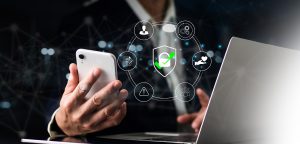 Person holding a smartphone and working on a laptop with a digital security interface overlay, symbolizing Top Cybersecurity Threats in 2025.